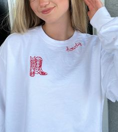 Introducing our "Howdy Embroidered Crewneck" - a fusion of comfort and Western charm that will effortlessly elevate your wardrobe. This exquisite white crewneck is not just an article of clothing; it's a statement piece that embraces the spirit of the frontier in a contemporary fashion. At the heart of this design lies the word "Howdy," hand embroidered in vibrant red cursive around the neckline. This subtle yet bold touch adds a warm and welcoming vibe, making it a perfect choice for casual outings and gatherings with friends. The real showstopper, however, is the finely detailed red cowboy boots embroidery adorning the right side of the chest. These intricate boots pay homage to the timeless allure of the Wild West, offering a tasteful nod to Western heritage while keeping the design mod White Sweatshirt With Custom Embroidery, Relaxed Fit, White Sweatshirt With Custom Embroidery In Relaxed Fit, Oversized Embroidered White Top, Oversized White Embroidered Top, White Custom Embroidery Relaxed Fit Tops, White Tops With Custom Embroidery Relaxed Fit, White Relaxed Fit Top With Custom Embroidery, White Embroidered Crew Top, White Embroidered Sweatshirt For Fall