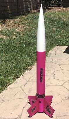 a pink and white rocket sitting on top of a cement slab in the grass next to a brick walkway