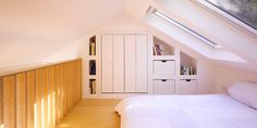 a bed sitting under a window in a bedroom next to a book shelf and cupboards