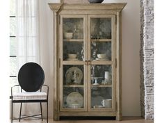 a glass door cabinet with dishes on top and plates in the bottom, next to a chair