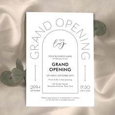 an open grand opening card on top of a white sheet with eucalyptus leaves in the foreground