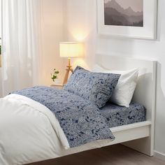 a white bed with blue and white comforter in front of a painting on the wall