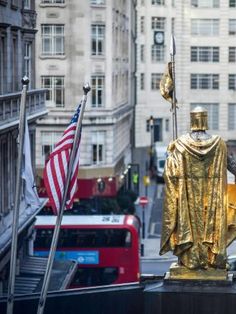 there is a golden statue in the middle of this city street with flags flying from it's sides