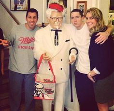 three people pose with a statue of a man holding a shopping bag