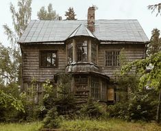 an old wooden house in the woods with overgrown trees around it and lots of windows