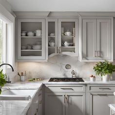 a kitchen with gray cabinets and marble counter tops, along with white dishes on the shelves