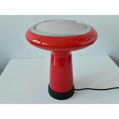 a red and white lamp sitting on top of a table next to a black cord