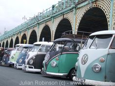 a row of vw buses parked next to each other in front of a bridge