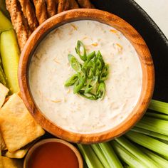 a wooden bowl filled with dip surrounded by crackers and celery