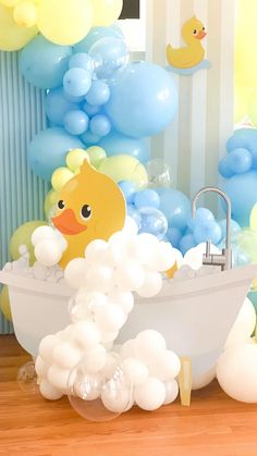 a bathtub filled with white and blue balloons next to a rubber duck floating in the tub