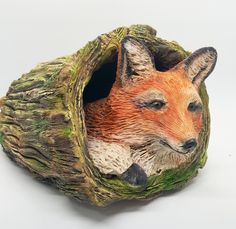 a figurine of a red fox resting in a tree stump with its eyes open