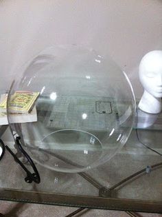 there is a glass table with a clear bowl on it and two white heads in the background