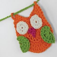 an orange crocheted owl ornament hanging from a green string on a white background