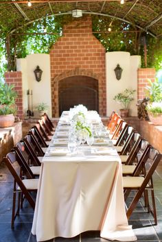 an outdoor dining area with tables and chairs set up for a formal dinner in front of a fireplace