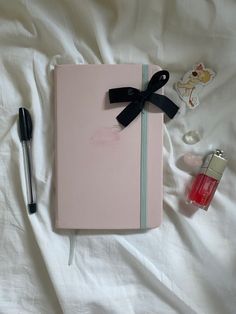 a pink notebook with a black ribbon and some other items laying on top of it