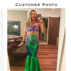 a woman in a green mermaid costume taking a selfie with her cell phone while standing in front of a bed