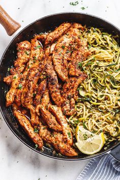 a skillet filled with chicken, noodles and lemon wedges