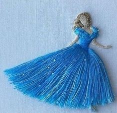 a blue dress is hanging on a white surface with beads and pearls in the shape of a woman's head