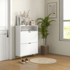 a white cabinet sitting next to a potted plant on top of a wooden floor