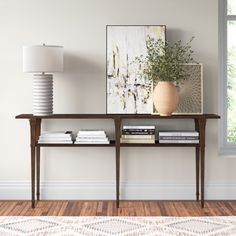 a living room with a table, lamp and pictures on the wall above it in front of a window