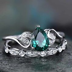 a ring with an emerald colored stone surrounded by white diamond accents on top of a rock