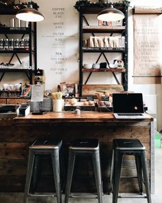 two laptops sitting on top of a wooden table in front of shelves with coffee cups