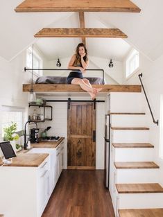 a woman sitting on top of a bed in a loft next to a kitchen and stairs