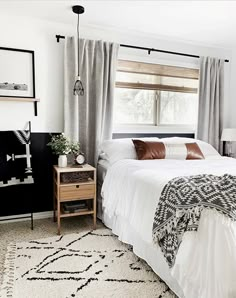 a bedroom with a white bed, black and white rugs, gray drapes, brown pillows