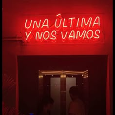 two people standing in front of a red neon sign that reads una ultima y nos vamos