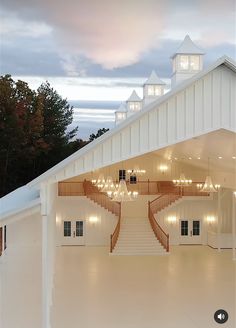 a large white building with stairs leading up to the top floor and lights hanging from the roof