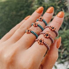 a woman's hand holding five rings with beads and stones on them, all in different colors