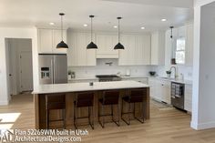 a large kitchen with white cabinets and wooden flooring is pictured in this image, there are three bar stools at the center of the island