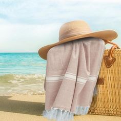 a woman's hat and blanket sitting on the beach next to an open suitcase