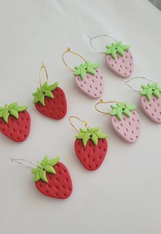 six strawberry shaped earrings with green bows on them sitting on a white counter top next to each other