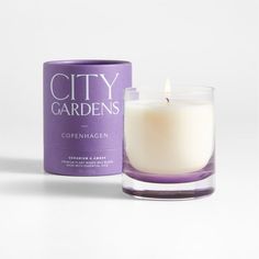 a candle that is sitting next to a box on a white surface with the words city gardens written in it