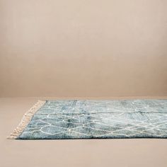 a blue and white rug with fringes on the floor in front of a beige wall