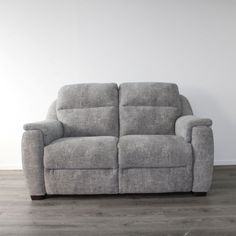 a grey reclining couch sitting on top of a wooden floor next to a white wall