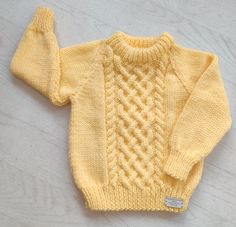 a yellow knitted sweater on a white wooden surface with a tag in the middle