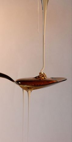 a spoon with liquid dripping from it on top of a white table next to a wall