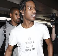 a man with dreadlocks is walking through an airport while another man holds onto his cell phone