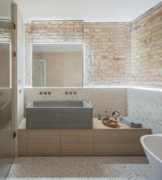 a bathroom with a sink, mirror and bathtub next to a brick walled wall