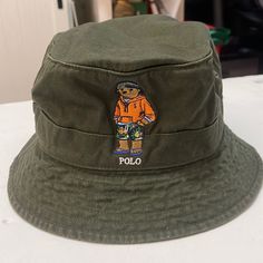 Nwt Polo Ralph Lauren Bear Green Bucket Hat Seamed Brim Sweatband At The Interior 1" Band Around The Crown Ralph Lauren's Polo Bear Embroidered At The Front Size S/M: 22¾" Inner Circumference. Size L/Xl: 24" Inner Circumference Cotton Spot Clean Brown Hats With Embroidered Logo For Summer, Brown Hat With Embroidered Logo For Summer, Brown Summer Hats With Embroidered Logo, Casual Wide Brim Hat With Embroidered Logo, Casual Khaki Bucket Hat With Flat Brim, Casual Green Hat Bands For Outdoor, Polo Beanie, Bear Bucket Hat, Polo Ralph Lauren Bear