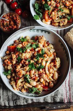 two bowls filled with pasta and vegetables on top of a table next to some bread