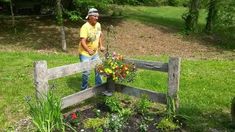 a man standing next to a wooden fence with flowers growing out of the ground in front of him