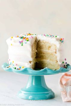 a cake with white frosting and sprinkles on a blue plate next to a pink napkin