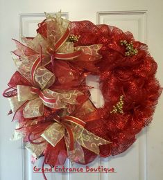 a red and gold mesh wreath on a white door with the words grand entrance boutique