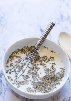 a bowl filled with milk and herbs next to a wooden spoon on a marble counter