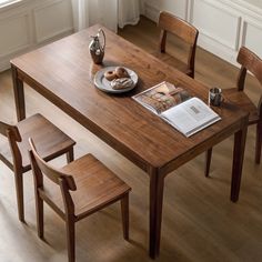 a wooden table with two chairs and a plate of food on it next to a window