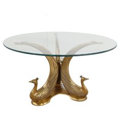 a glass and brass table with two birds on the base, against a white background