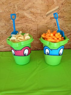 two cups filled with food sitting on top of a green tablecloth covered table next to a wooden wall